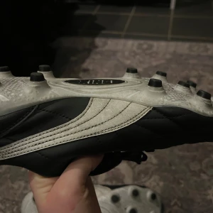 Svarta fotbollsskor Puma King - Säljer ett par klassiska svarta Puma King fotbollsskor med vit logga och snörning. Skorna har dobbar för bra grepp på planen och är tillverkade i skinn för en bekväm passform. Ag/fg skor.