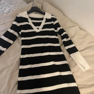 Svart och vit randig klänning - Snygg svart och vit randig klänning med v-ringad hals och långa ärmar. Perfekt för en stilren look. Klänningen har en ribbad struktur som ger en skön passform.