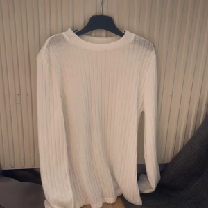 Vit ribbad långärmad tröja - Säljer en stilren vit ribbad tröja med lång ärm och rund halsringning. Tröjan är mjuk och stretchig, perfekt att matcha med jeans eller kjol. Enkel och tidlös design som passar till många olika outfits.