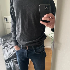 Mörkgrå stickad tröja - En enkel och stilren mörkgrå stickad tröja med rund halsringning och långa ärmar. Perfekt att matcha med jeans eller chinos för en clean look.
