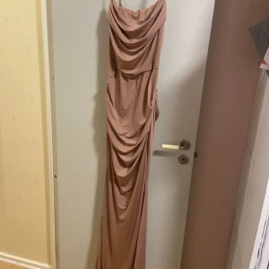 Ljus rosa  långklänning  - Säljer en elegant ljusrosa långklänning med draperad framsida och smala axelband. Klänningen har en figurnära passform och en vacker omlottliknande effekt framtill. Perfekt för speciella tillfällen. Har endast används en gång och är väldigt fin på, skriv om ni har frågor:)