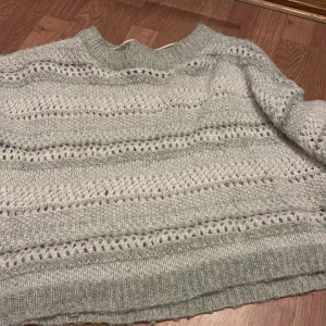 Ljusgrå stickad tröja med hålmönster - Mysig ljusgrå stickad tröja med hålmönster och ribbade muddar. Tröjan har lång ärm och en avslappnad passform, perfekt för kyliga dagar. Passar till många olika stilar och är superbekväm.