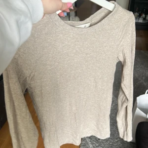 Beige långärmad tröja från H&M - En enkel och stilren beige långärmad tröja från H&M. Tröjan har rund halsringning och är tillverkad i ett mjukt bomullsmaterial. Perfekt att bära som basplagg eller under en kofta.