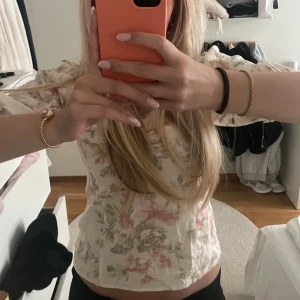 Blommig offshoulder blus i pastellfärger - Söt offshoulder blus i linne material med blommigt mönster i ljusa pastellfärger. Toppen har korta ärmar och en smickrande passform, perfekt för varmare dagar. 