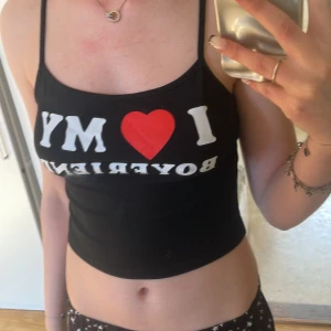 Svart croppad linne med text - Säljer ett svart croppat linne med tunna axelband och trycket 'I ❤️ MY BOYFRIEND' i vitt och rött framtill. Perfekt för en avslappnad och trendig look.