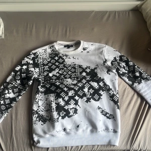 Vit och svart sweatshirt från Louis Vuitton - Säljer en vit sweatshirt från Louis Vuitton med svart, abstrakt mönster och klassiska LV-loggor över hela tröjan. Väldigt unik tröja vilket gör att det sticker ut från resten av alla basic kläder från dyra märkeskläder. Storleken är L men tröjan är liten i storleken så passformen är S-M