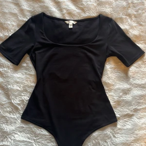 Svart body från H&M - Svart body från H&M med rundad urringning och korta ärmar. Bodyn har knäppning i grenen och är tillverkad i ett mjukt, stretchigt material som sitter tight mot kroppen. Perfekt att styla med jeans eller kjol.
