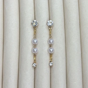 Guldiga örhängen med pärlor och stenar - Säljer ett par eleganta örhängen i guldton med två vita pärlor och gnistrande stenar upptill och nedtill. Perfekta för att lyfta din look med en touch av glamour.