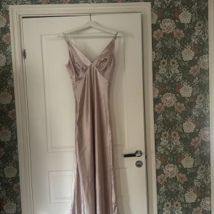 Ljusrosa balklänning från Boohoo - Säljer en elegant ljusrosa långklänning från Boohoo i glansigt satinmaterial. Klänningen har smala axelband och v-ringad urringning framtill. Perfekt för speciella tillfällen när du vill känna dig extra fin.