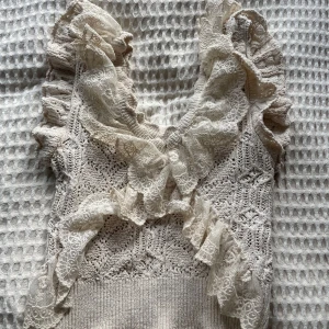 Beige stickad topp med spetsvolanger från Zara - Supersöt beige stickad topp från Zara med breda spetsvolanger längs axlar och ringning. Toppen har ett vackert mönsterstickat material och romantiska detaljer som ger en feminin look.