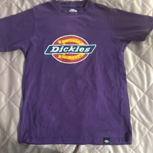 Lila t-shirt från Dickies med logga - Säljer en lila t-shirt från Dickies med stor färgglad logga framtill. Klassisk passform och rund halsringning. Perfekt för dig som gillar streetwear och vill ha en färgklick i garderoben.
