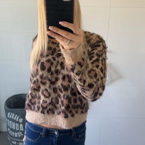 Beige leopardmönstrad croppad stickad tröja - Säljer en beige stickad tröja med leopardmönster. Tröjan är croppad och har långa ärmar samt ribbade muddar vid ärmslut och nederkant. Perfekt för dig som gillar djurmönster och vill ha en mysig men trendig look 💕