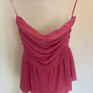 Rosa sommartopp med broderade detaljer - Söt rosa offshoulder sommartopp. Toppen har broderade blommönster och en luftig, lätt volang nertill. Perfekt för varma dagar och somriga tillfällen.