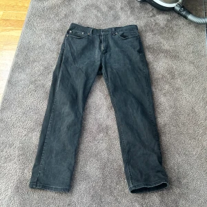 Svarta Levis 541 - Klassiska svarta jeansbyxor från Levi's med fem fickor och raka ben. Byxorna har normal passform och är tillverkade i ett robust jeanstyg. Perfekta för en stilren och enkel look. Storlek 34/30.