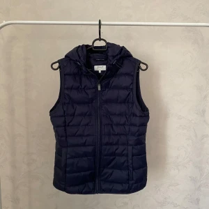 Mörkblå dunväst med huva från ONLY - Säljer en mörkblå dunväst från ONLY med huva och dragkedja framtill. Knappt använd!