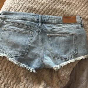 Ljusblå lågmidjade jeansshorts med fransar och paisleydetaljer - Säljer ett par jättesnygga ljusblå jeansshorts med slitna detaljer, fransig kant och röda paisleymönstrade tygdetaljer i fickorna. de är i storlek S och jag säljer pågrund av att de tyvärr inte passar på mig längre. Klassisk femficksmodell med knapp och dragkedja. Perfekta för sommaren!🥰🥰🥰 Skriv gärna