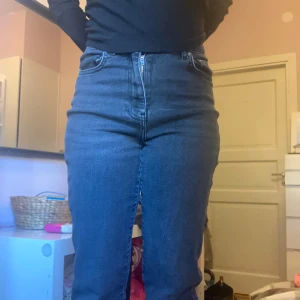 Gråsvarta jeansbyxor från Gina Tricot - Säljer ett par gråsvarta jeansbyxor från Gina Tricot med hög midja. Jeansen har raka ben och stängs med dragkedja och knapp. Perfekta för en stilren vardagslook.