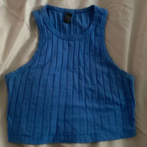 Blå ribbad croppad linnetopp - Säljer en blå croppad linnetopp med ribbad struktur. Toppen är ärmlös och har en rund halsringning. Perfekt för varma dagar eller som ett lager under en skjorta.