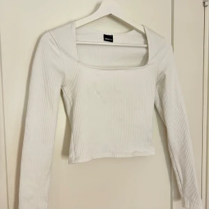 Vit ribbad långärmad topp från Gina  - Säljer en vit ribbad långärmad topp från Gina med fyrkantig ringning. Toppen är croppad och har en tight passform, perfekt att styla med jeans eller kjol.