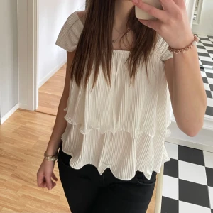 Vit volangtopp - Säljer en söt vit blus med plisserat tyg och volangdetaljer. Blusen har korta ärmar och en luftig, lös passform. Perfekt att matcha med jeans eller kjol.💗