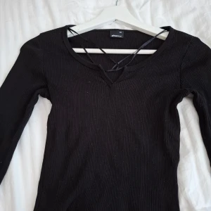 Svart ribbad tröja med snörning från Gina Tricot - Säljer en svart långärmad ribbad tröja från Gina Tricot i storlek XS. Tröjan har v-ringning och dekorativ snörning framtill. Perfekt till många olika outfits!
