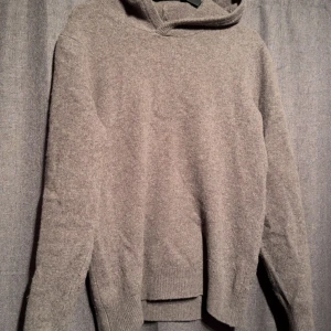 Grå hoodie i merinoull från Vailent - Mysig brun/grå hoodie från Vailent i mjuk merinoull. Tröjan har lång ärm, huva och ribbade muddar vid ärmslut och nederkant. Perfekt för kyliga dagar när du vill vara både bekväm och snygg. 100% merinoull. Pris kan diskuteras.