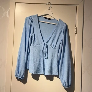 Ljusblå blus med knyt från Bik Bok - Supersöt ljusblå blus från Bik Bok med v-ringning och knyt framtill. Långa ärmar med lätt puff och resår vid ärmslut. Perfekt för vår och sommar!