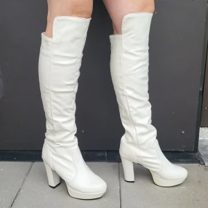 Vita/ivory/benvita overknee stövlar med klack - Säljer ett par höga vita/ivory/benvita overknee stövlar med rejäl klack och platåsula. Skorna har rund tå och är tillverkade i syntetmaterial. Perfekta för dig som vill sticka ut med ett statement-plagg. Endast använda en gång, inomhus. Stövlarna har små skavanker (se bild),men i fint skick. Fler bilder kan skickas.