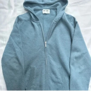Ljusblå hoodie från Soft Goat - Mysig ljusblå hoodie från Soft Goat i mjukt material. Tröjan har dragkedja framtill, två fickor och långa ärmar. Storlek 170, nypris 2000kr i 100% cashmere.