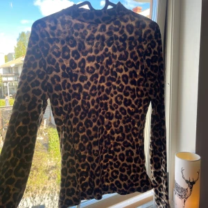 Leopardmönstrad långärmad topp från Hailys - Säljer en snygg långärmad topp från Hailys i leopardmönster. Toppen är figurnära och har en rund halsringning. Perfekt för dig som vill sticka ut lite extra med ett djurmönster!