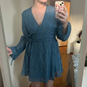 Blå omlottklänning med detaljer - Superfin blå omlottklänning med diskret mönster och fina detaljer, använd 1 gång. Nypris var 599 SEK men klänningen säljs inte längre 💙