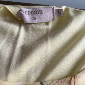 Gul blommig klänning från Cream - Söt gul klänning från Cream med blommigt mönster i rosa, lila och grönt. Klänningen har trekvartsärmar och volang nertill, samt en avslappnad passform. Perfekt för vår och sommar!
