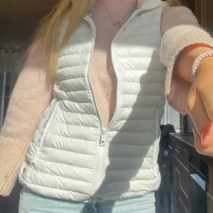 Vit dunväst från Colmar - Säljer en snygg och lätt vit dunväst från Colmar. Västen har dragkedja framtill och två fickor med dragkedja på sidorna. Perfekt att slänga över en stickad tröja för en fräsch look. Passar till många olika outfits!