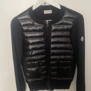 Svart puffer cardigan jacka från Moncler - Säljer en svart cardigan jacka från Moncler med glansig pufferfront och två fickor framtill. Jackan har långa ärmar i stickad kvalitet och dragkedja. Klassisk Moncler-logga på ärmen och rund halsringning.💖 om ni vill ha mer bilder skriv till mig💖