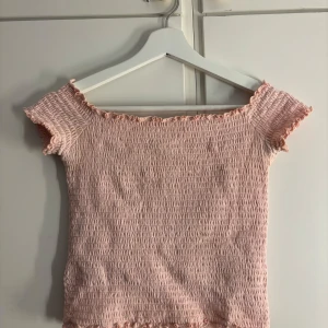 Ljusrosa smockad topp från Hollister - Supersöt ljusrosa smockad topp från Hollister med korta ärmar och volangdetaljer vid ärmslut och nederkant. Står att den är i storlek M men sitter mer som en S. Kommer tyvärr inte till användning längre💕 
