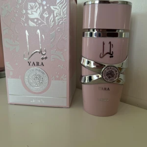 Yara Eau de Parfum från Lattafa - Yara är en parfym i en ljusrosa flaska med silverdetaljer och arabiska bokstäver på framsidan. Flaskan har en modern, stilren design och kommer i en matchande ask med blommönster och silverinslag. Ca halva kvar, pris kan diskuteras vid snabb affär 