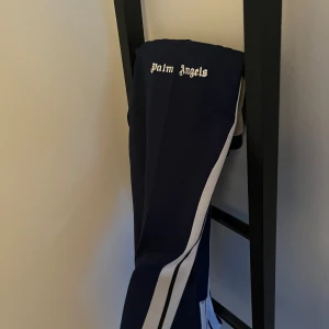 Mörkblå byxor från Palm Angels med vita ränder - Snygga mörkblå byxor från Palm Angels med vita sidoränder och logga framtill. Byxorna har en sportig look 