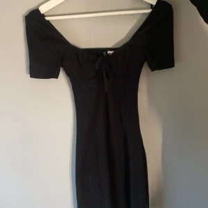 Svart offshoulder klänning från Divided - Säljer en svart offshoulder klänning från Divided i storlek XXS. Klänningen har korta ärmar och en söt knytdetalj framtill. Perfekt för dig som gillar en enkel men stilren look.