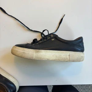 Svarta sneakers från Wesc - Säljer ett par svarta sneakers från K.Cobler med vit platt sula och snörning. Skorna har rund tå och guldiga öljetter för snörena. Perfekta för en stilren vardagslook. Nypris 1300 kr