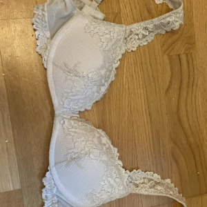 Beige/vit spets-bh från Intimissimi - Säljer en vit bh från Intimissimi med fina spetsdetaljer längs kanterna. Bh:n har vadderade kupor och justerbara axelband. Perfekt för dig som vill ha en klassisk och feminin look. Vet inte helt säkert eftersom lappen är bortklippt men gissar på att storleken är 75b! Den har en liten fläck inuti som synd på bild 2