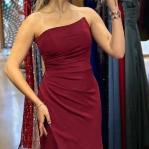 Mörkröd axelbandslös långklänning - Vinröd balklänning med figurnära passform. Klänningen har slits framtill och är tillverkad i ett slätt, lätt glansigt material som ger en lyxig känsla. Perfekt för bal eller festliga tillfällen!💕🥰Klänningen är aldrig använd, prislappen är kvar🫶🏼