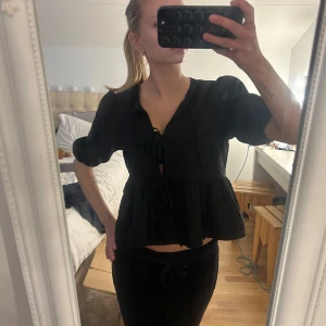 Svart topp - Snygg svart topp med trekvartsärm och knytband framtill. Perfekt för att lägga till en stilfull touch till din outfit. Passar bra till både vardag och fest!