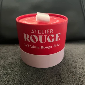 Atelier Rouge Je T’aime Rouge Trio - Snyggt set med tre nagelprodukter från Atelier Rouge i en rund röd och rosa ask. Innehåller ett mörkrött nagellack, en top coat och en base coat, alla med vita korkar. Perfekt för dig som vill mixa klassiska och edgy nagellooks.
