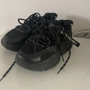 Chunky svarta sneakers med meshdetaljer - Svarta chunky sneakers med coola meshpaneler och robust sula. Skorna har svarta snören med vita detaljer och en tydlig logga på sidan. Perfekta för dig som gillar streetstyle och vill sticka ut med en modern look. Oanvänta tyvärr för små för mig:/