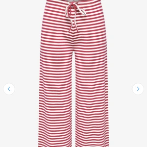 Randiga vida byxor med snörning - Säljer ett par röda och vita randiga byxor med breda ben och snörning i midjan. Byxorna har en avslappnad passform och är perfekta för en chill look. Materialet känns mjukt och bekvämt, och midjan är elastisk för extra komfort från Lindex! Följer även med en matchande långärmad tröja till.
