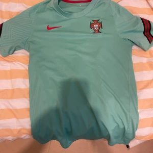 Portugal fotbollströja Nike S - Snygg Portugal fotbollströja från Nike i ljusgrön färg med röd Nike-logga och broderat landslagsemblem på bröstet. Tröjan har korta ärmar med svarta och röda detaljer och är tillverkad i Dri-Fit material som andas.