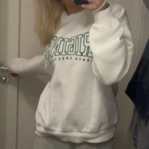 Vit sweatshirt med grön text - Vit sweatshirt med grön text 'ORIGINAL TRACK CHALLENGE' framtill. Tröjan har en avslappnad passform, rund halsringning och långa ärmar med ribbade muddar. Perfekt för en chill och sportig look.