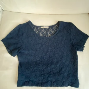 Mörkblå ungdoms  spetsblus från Pieces - Säljer en mörkblå, croppad blus från Pieces med korta ärmar. Toppen är helt täckt av blommig spets och har rund halsringning. 