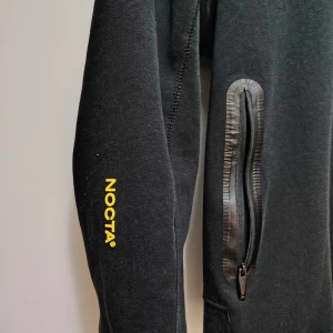 Svart NOCTA x Nike hoodiejacka M - Svart hoodiejacka från Nike NOCTA med hel dragkedja, två fickor med dragkedja och gul NOCTA-logga på ärmen. Snygg gul Nike Swoosh på bröstet. Jackan är i mjukt bomullsmaterial och har en clean, sportig vibe. Storlek m men passar också som S