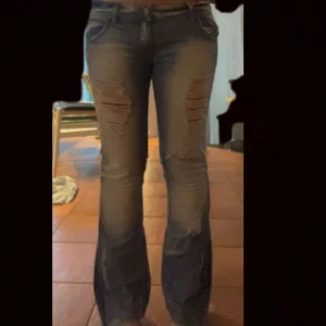 Blå slitna bootcut jeans - Säljer ett par blå bootcut jeans med slitningar och hål på låren och knäna. Jeansen har en ljus tvätt och klassisk femficksdesign. De är tillverkade i jeansmaterial och har en snygg, avslappnad vibe. Jag har sytt ut dom från skinny till bootcut med inget som syns tydligt 